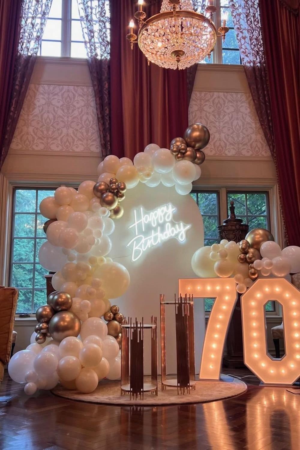 Large illuminated number 70 and a white balloon arch with neon Happy Birthday sign.