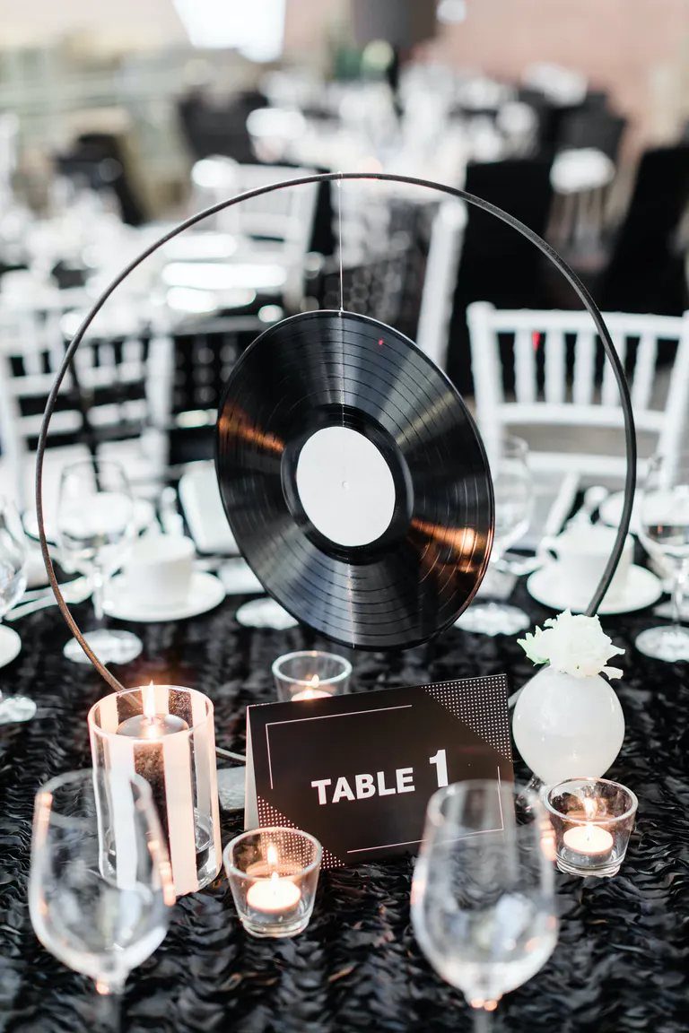 A black vinyl record centerpiece hanging in a metal ring on a formal black table setting.