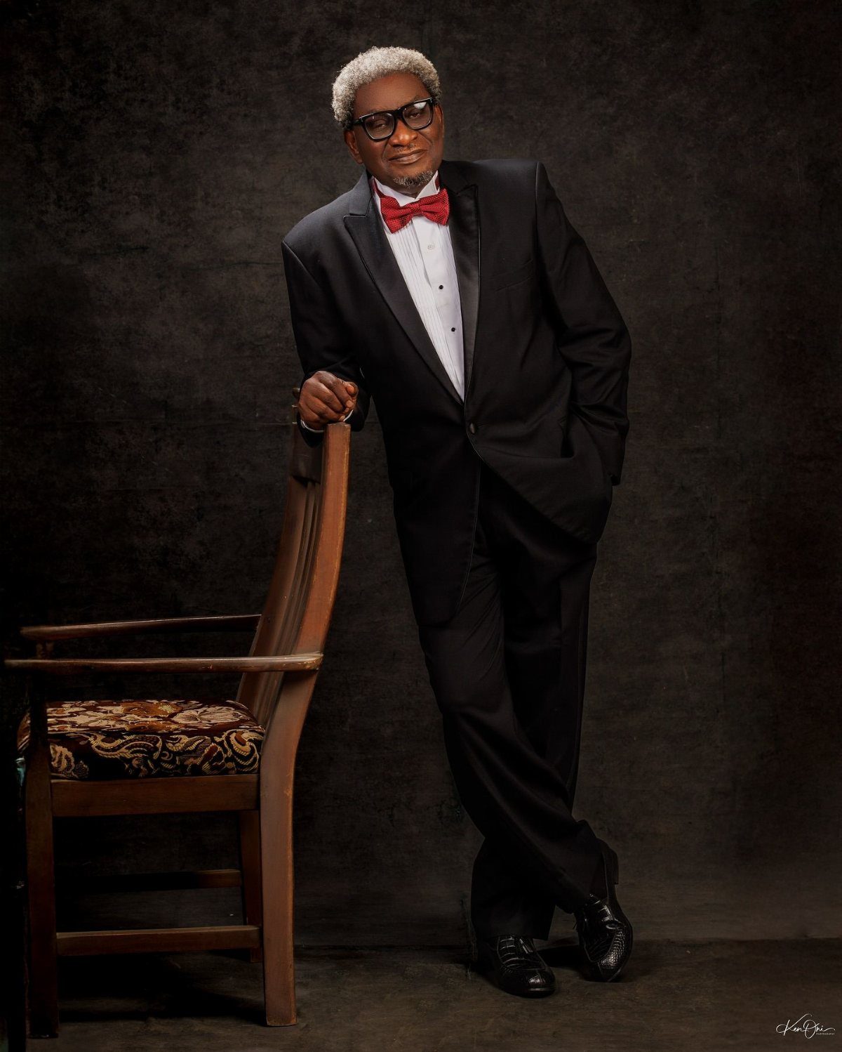 A senior man in a black tuxedo and red bowtie posing for a professional portrait.