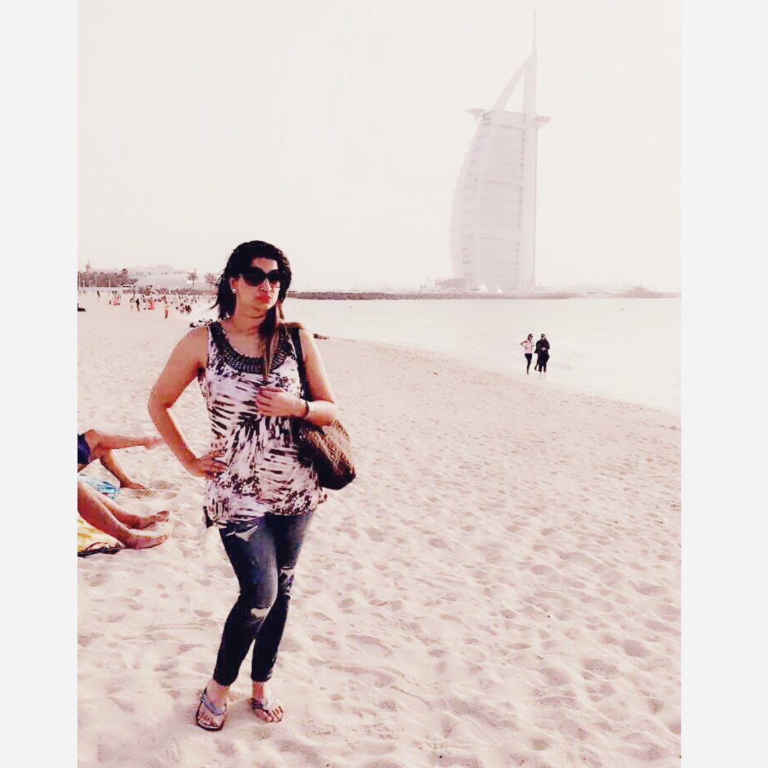 Woman posing on a beach with the Burj Al Arab hotel in the background.