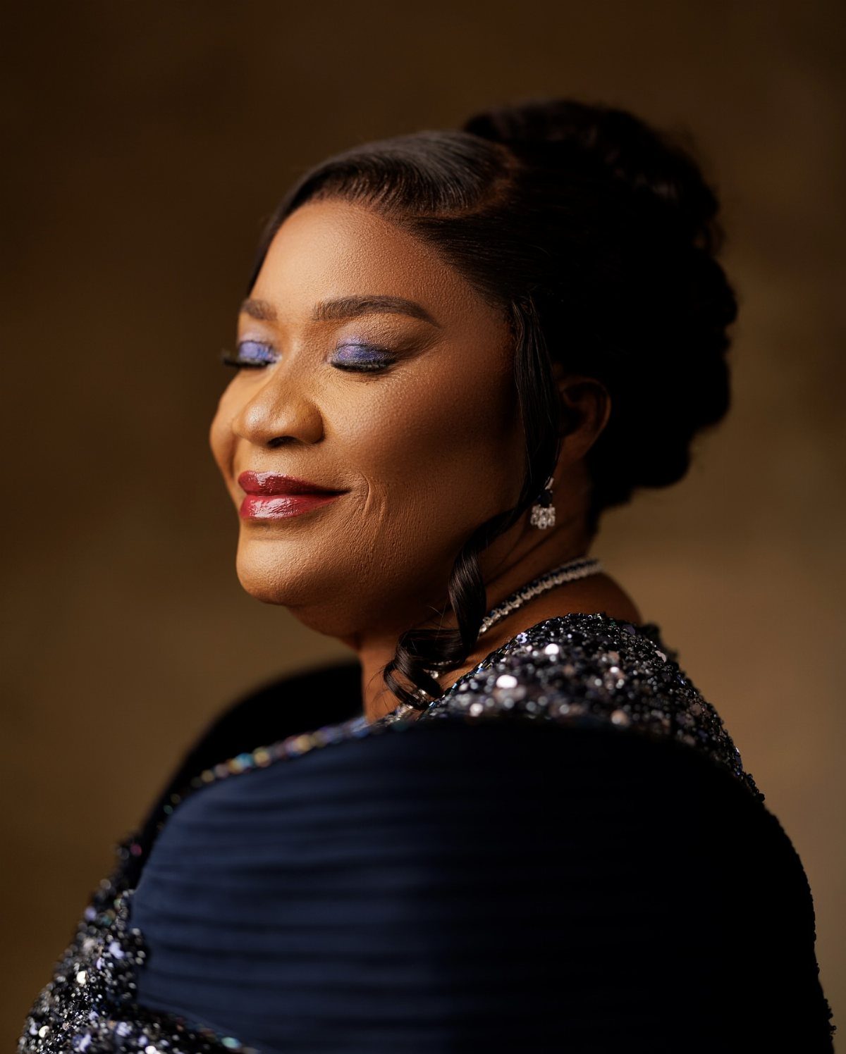 A smiling woman with blue eyeshadow and a sequined dress posing for a portrait.