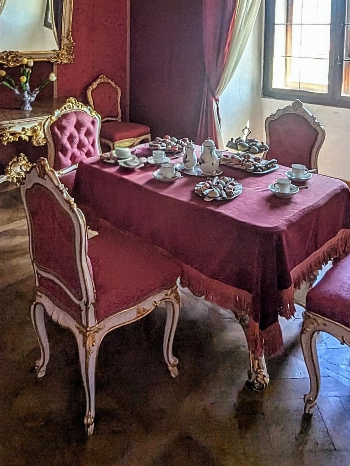 A formal table set for high tea with red linens, ornate chairs, and various pastries.