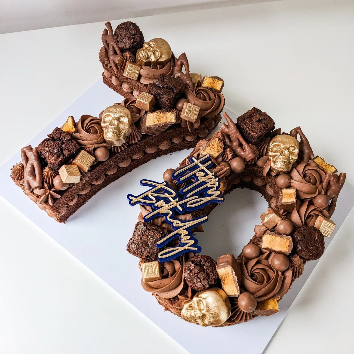 Chocolate cake numbers shaped like eighty decorated with brownies, gold skulls, and chocolate truffles.