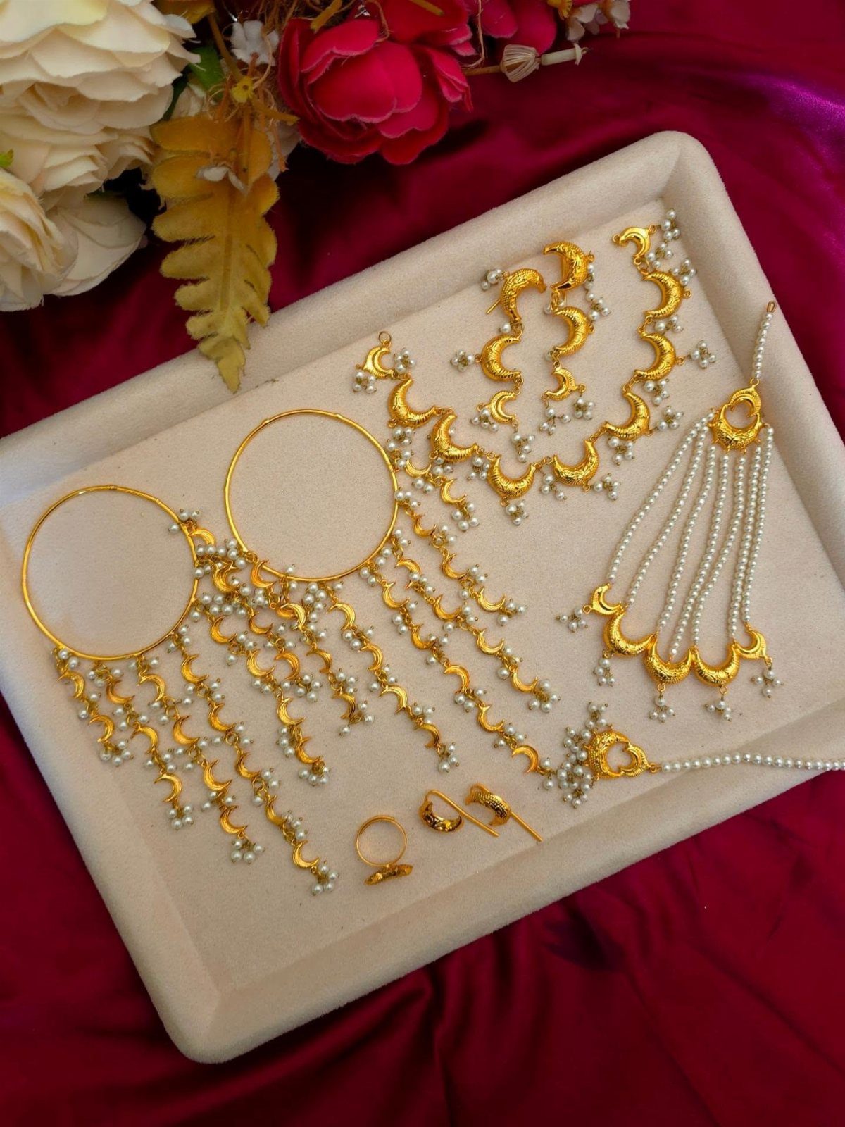 Ornate gold and pearl jewelry set arranged on a cream tray with floral accents.