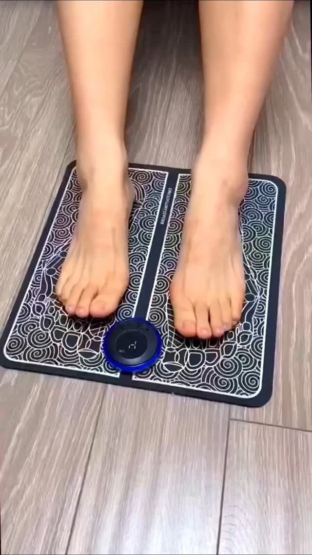 Bare feet resting on a patterned black and white foot massage mat on a wooden floor.