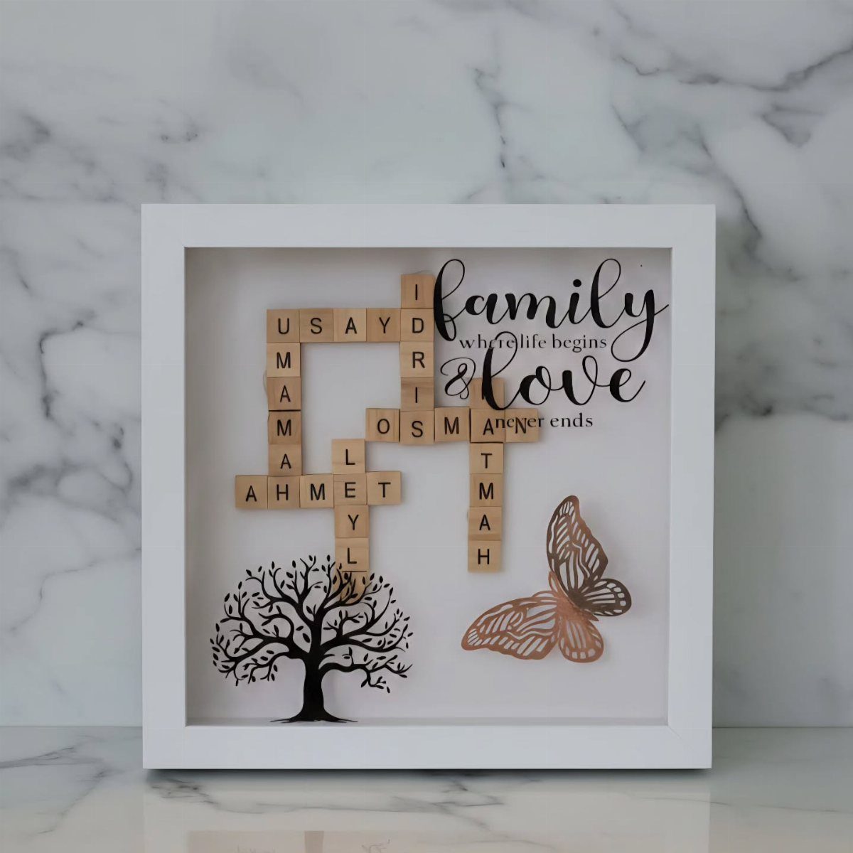 Wooden letter tiles in a crossword pattern next to a tree silhouette and butterfly inside a white frame.