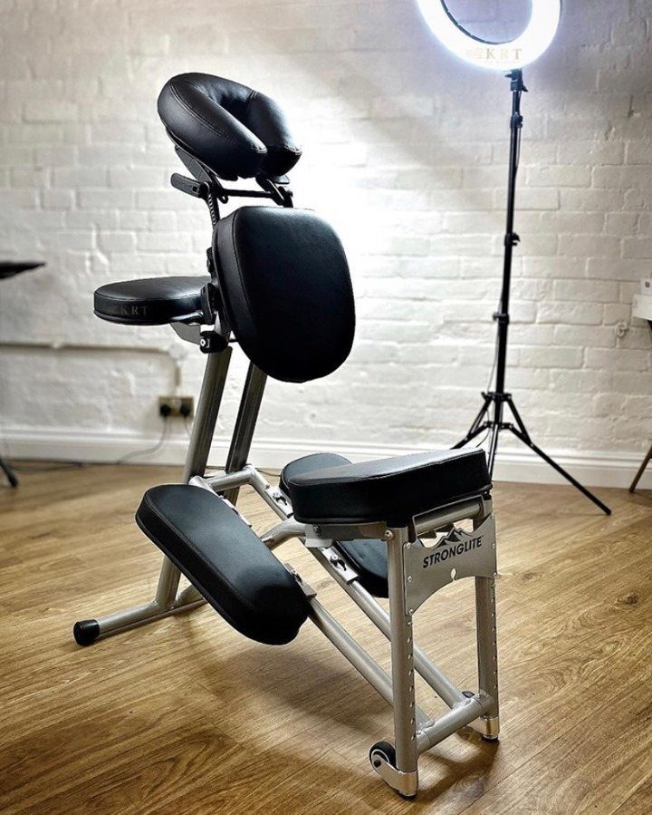 A black and silver portable massage chair positioned on a wooden floor indoors.