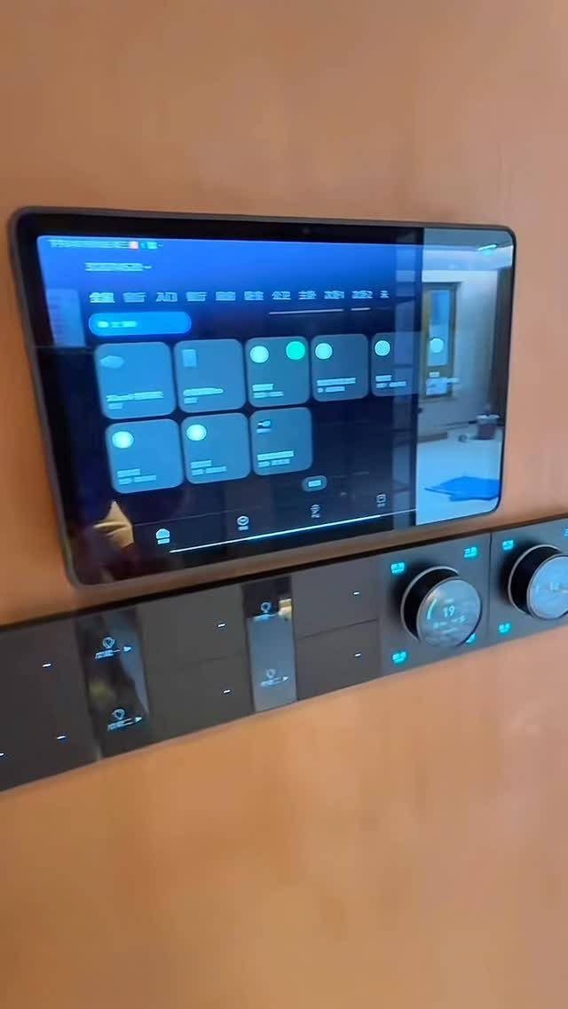 Digital tablet mounted on a wall displaying a smart home control interface with blue icons.