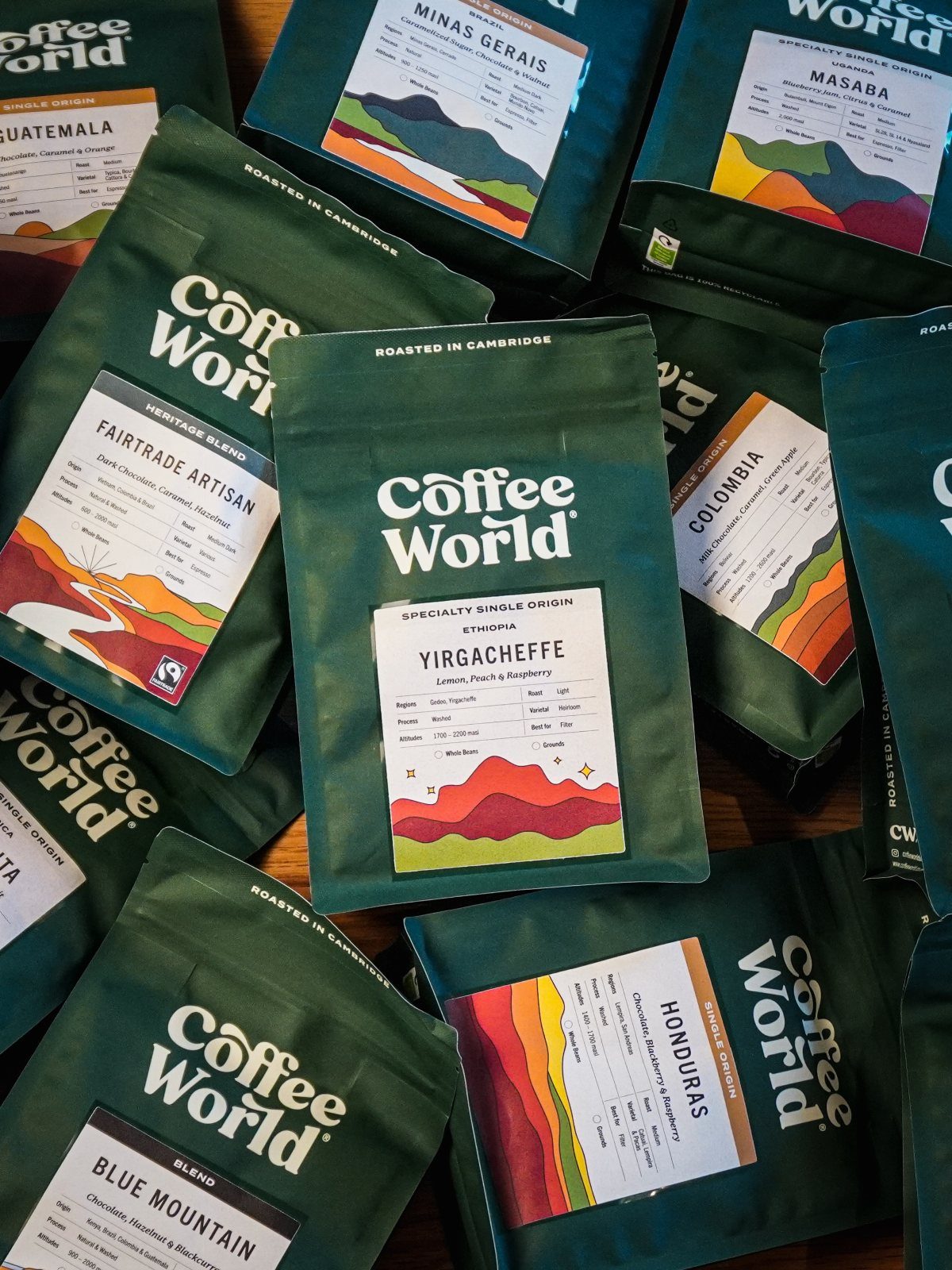 Multiple green bags of Coffee World specialty single origin coffee beans scattered together.