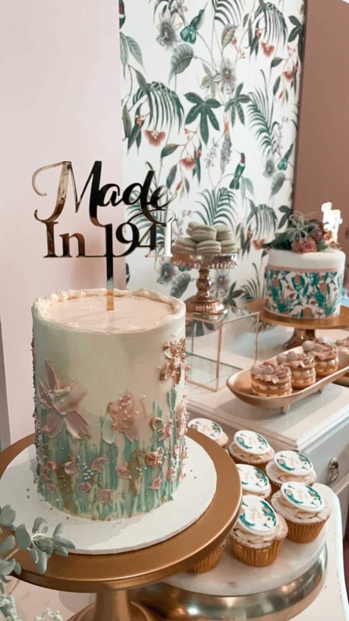 A light green floral cake with a gold Made In 1941 topper on a dessert table.