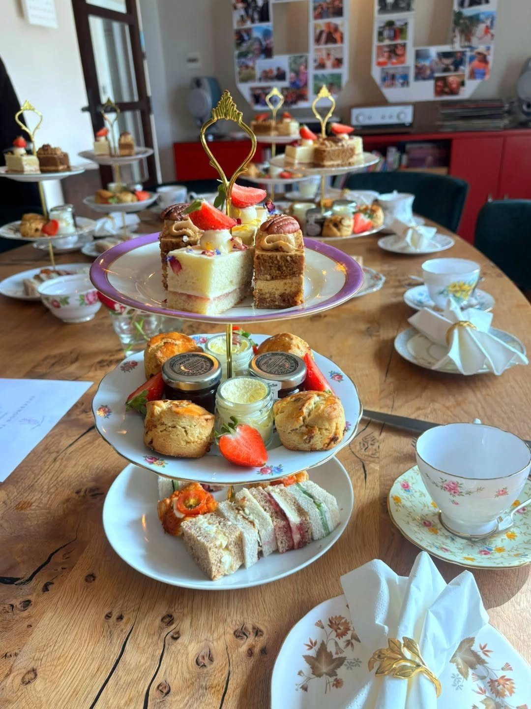 Tiered afternoon tea stands with sandwiches, scones, and cakes on a wooden table.