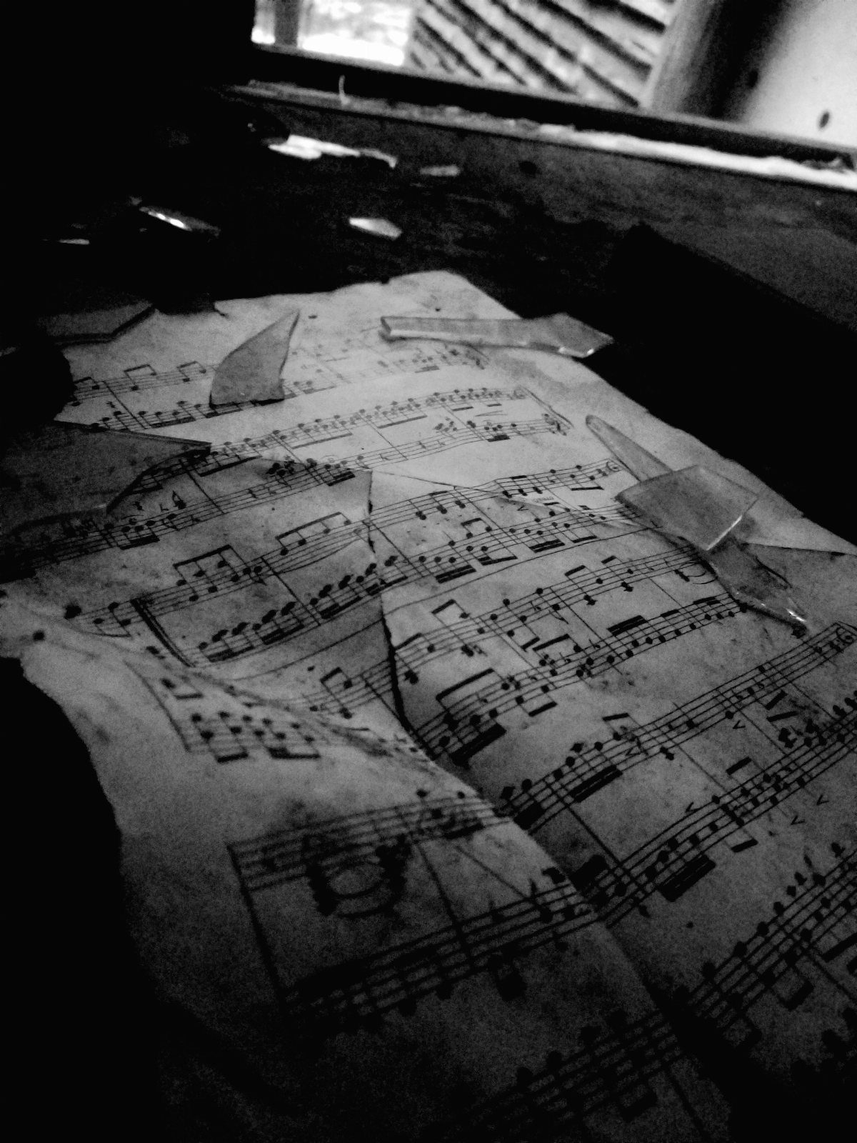 Torn and crumpled vintage sheet music scattered across a dark, textured surface in black and white.