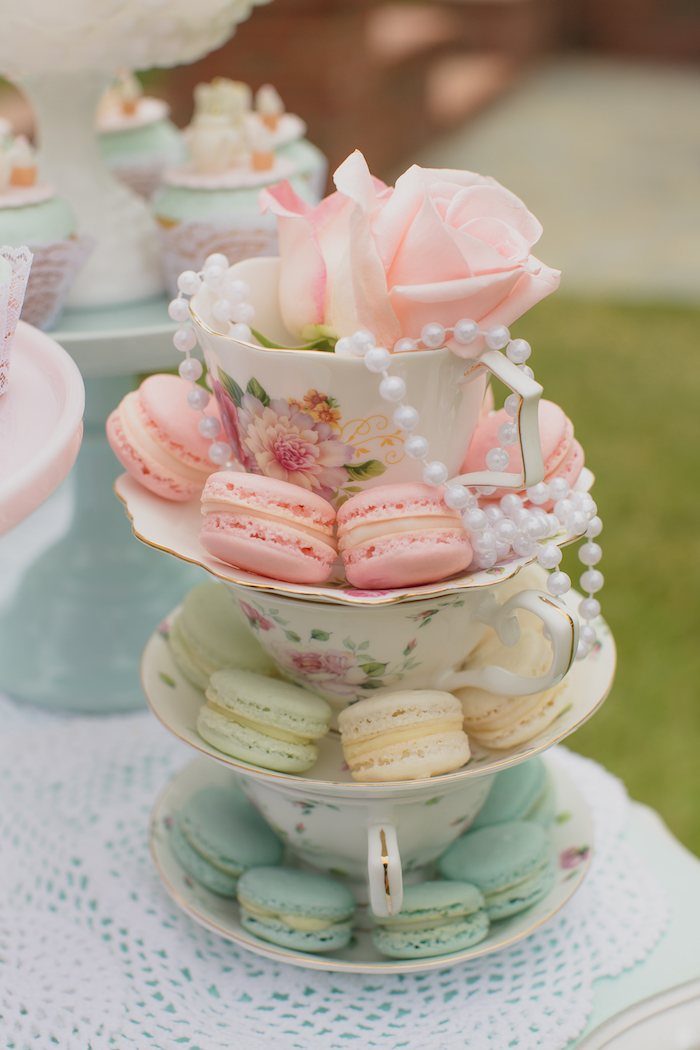 Stacked floral teacups filled with colorful macarons, decorated with a pink rose and white pearls.