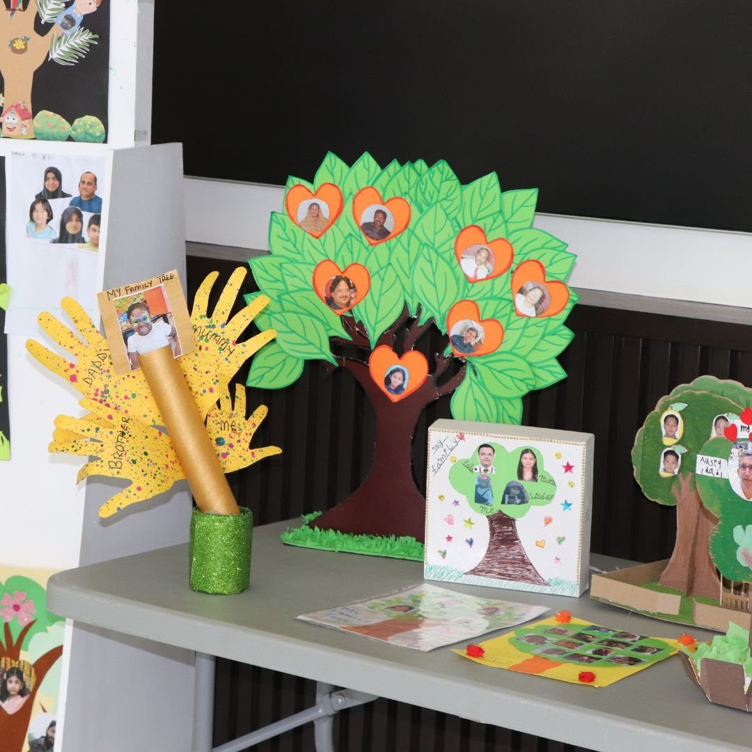 A green paper tree decorated with small heart-shaped family photographs on a grey table.