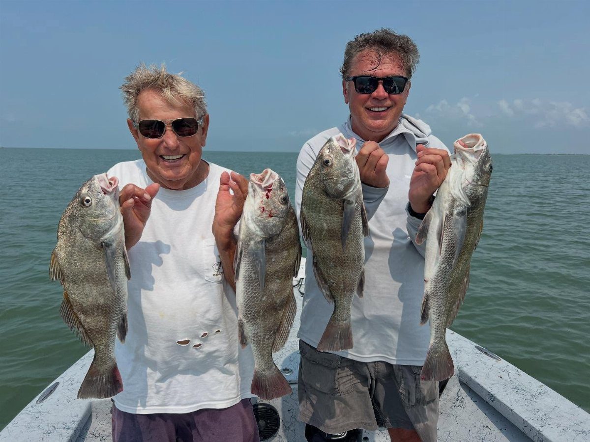 Two men smiling on a boat while holding up their fresh fish catch.