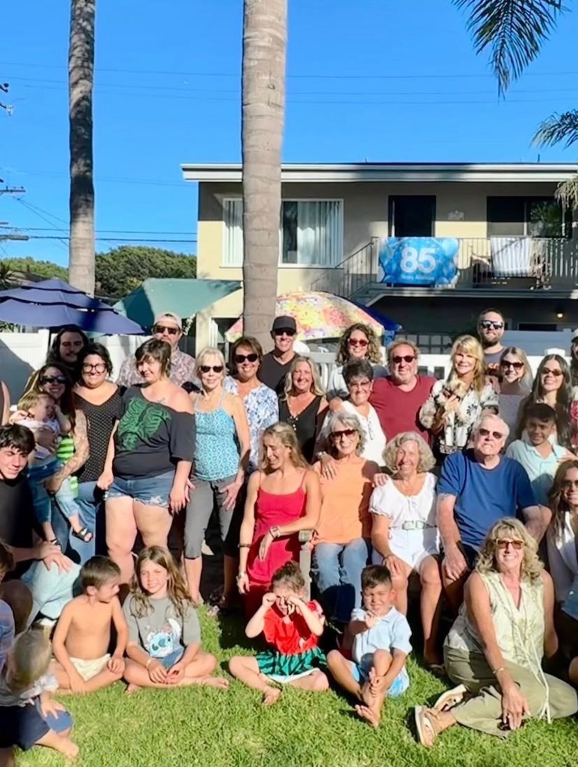 A large multi-generational group of people posing together on a sunny lawn outdoors.
