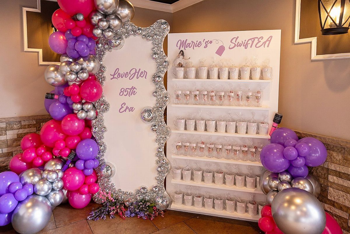 Pink and purple balloon arches surrounding a silver frame and a dessert display shelf.