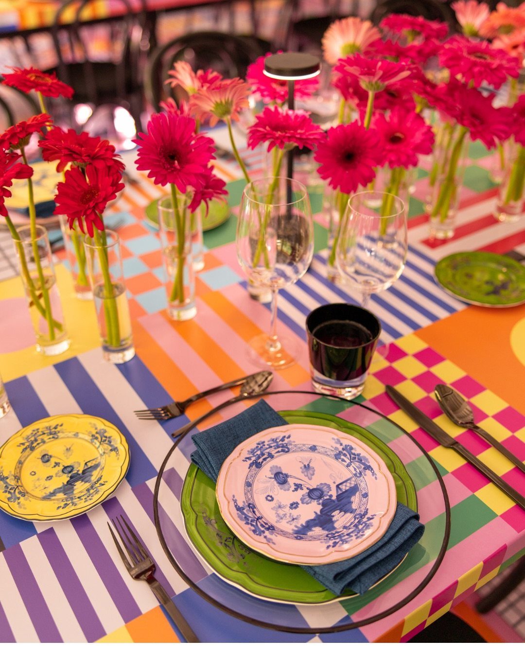 Colorful table setting with pink gerbera daisies, patterned plates, and striped tablecloths for a festive celebration.