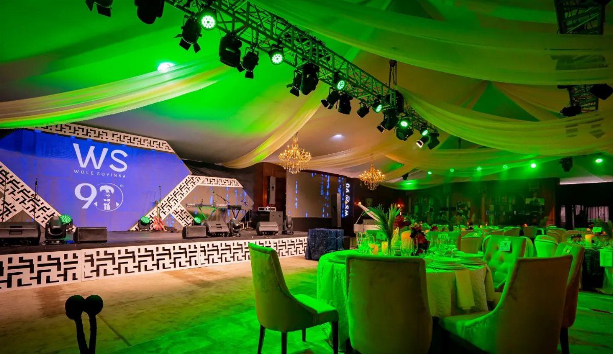A large banquet hall decorated with green lighting, draped ceilings, and a stage for a celebration.