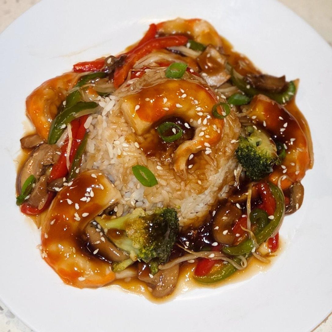 Shrimp and vegetable stir fry served over white rice on a white plate.