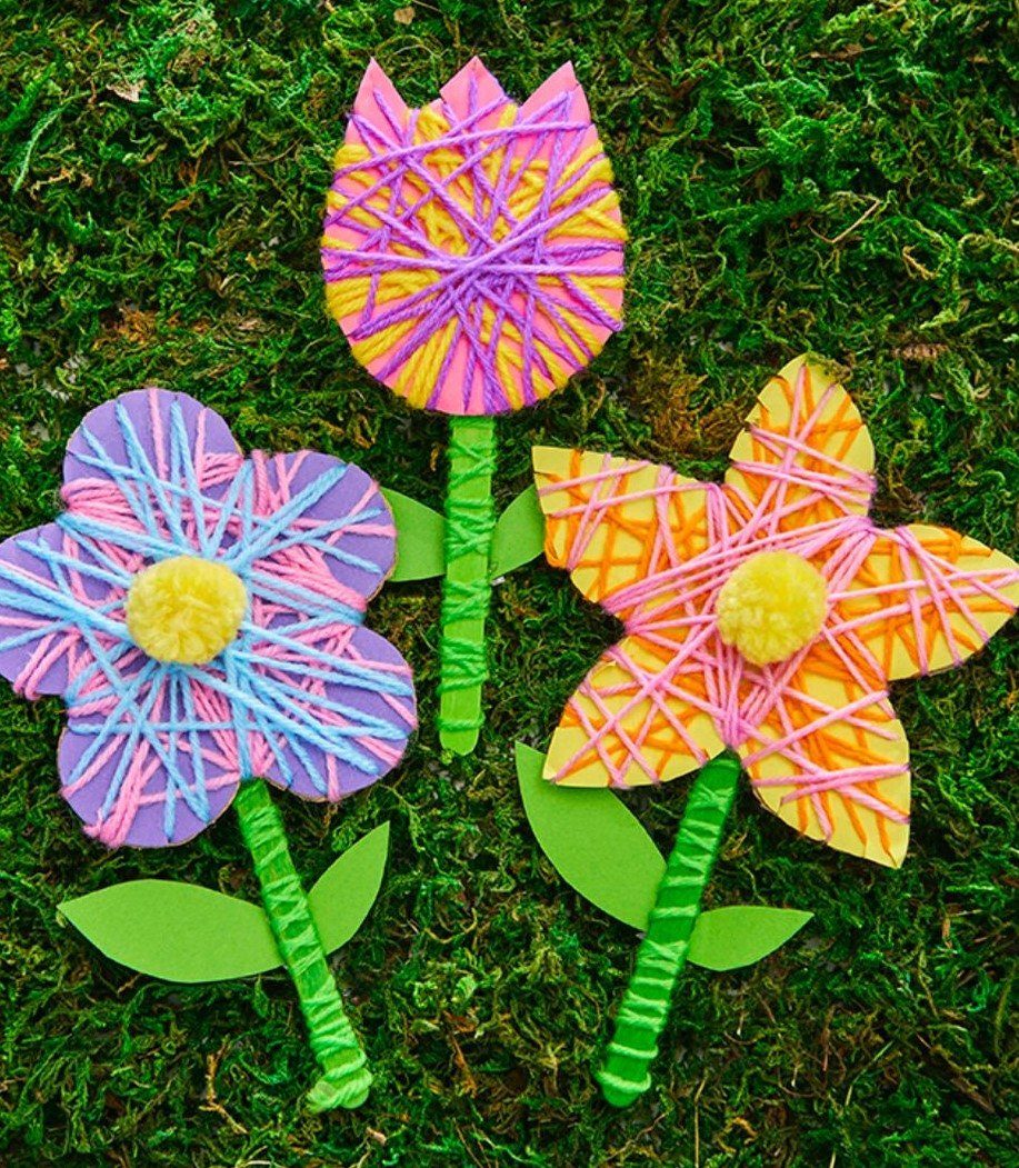 Three colorful handmade string art flowers resting on a bed of green moss.