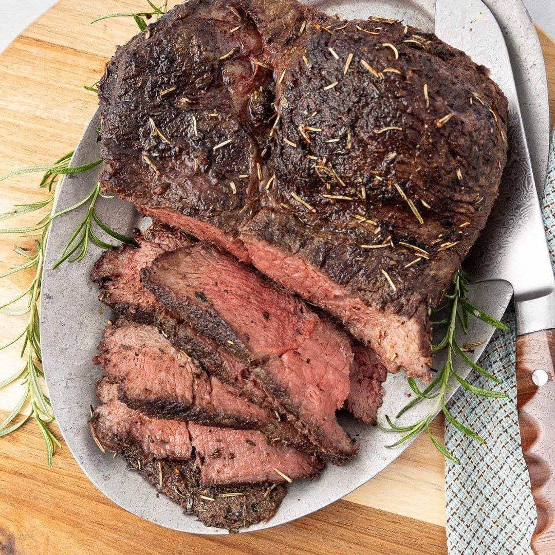 Sliced rosemary-seasoned roast beef served on a silver platter atop a wooden board.
