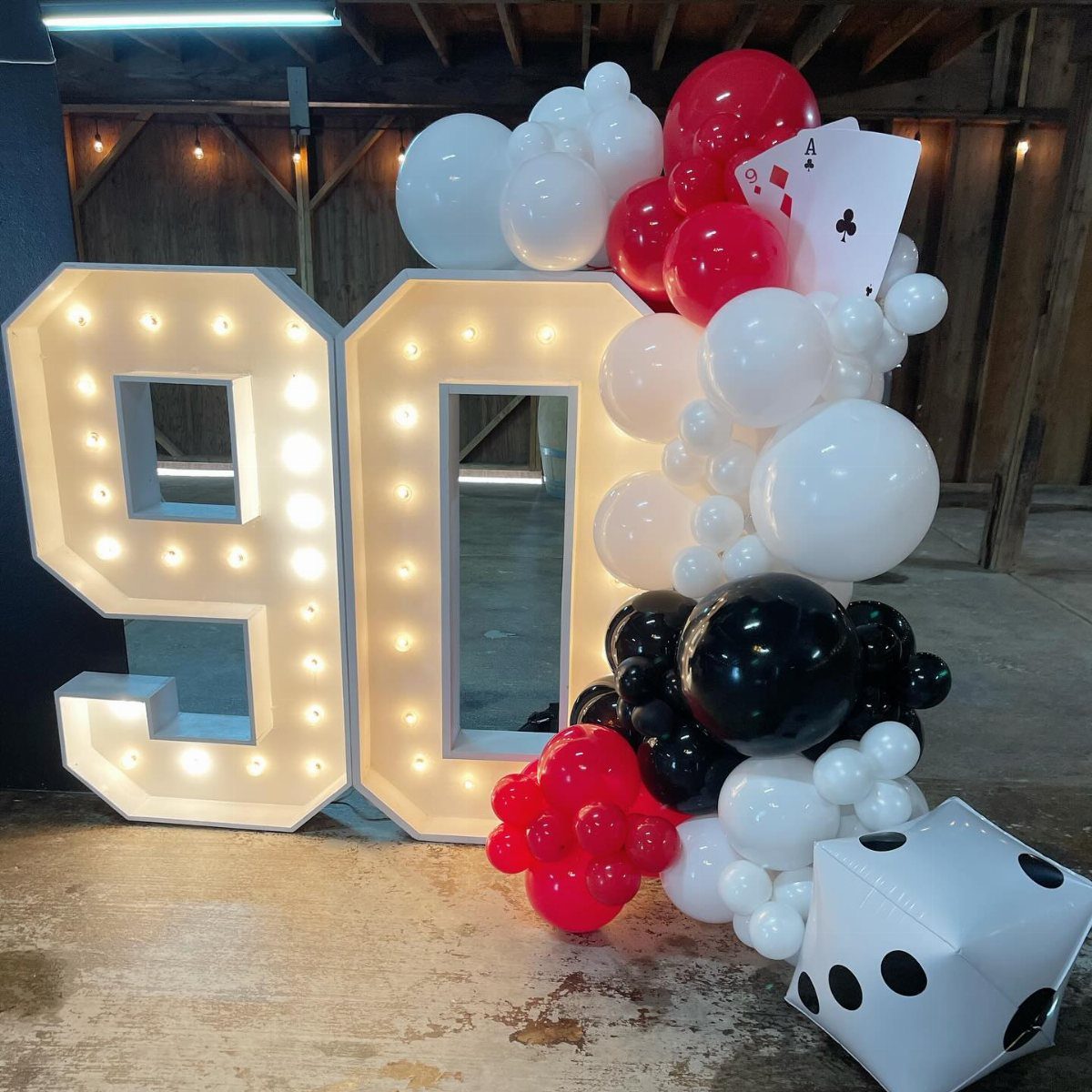 Large marquee light-up numbers ninety surrounded by red, white, and black balloons.