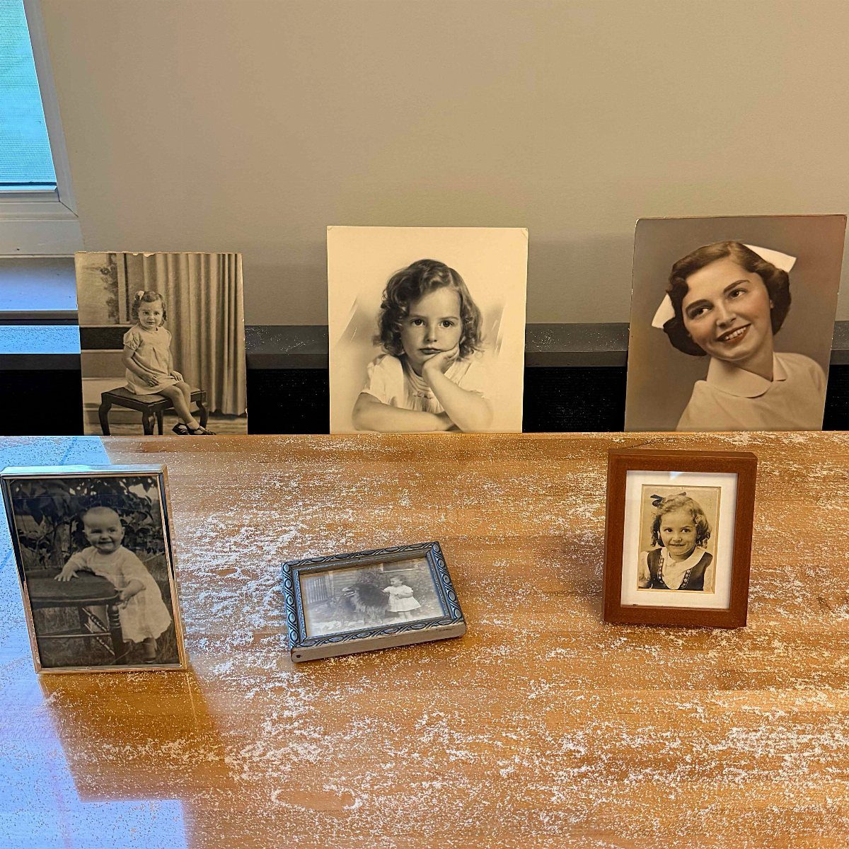 Vintage photographs of a young girl and woman displayed on a wooden table.