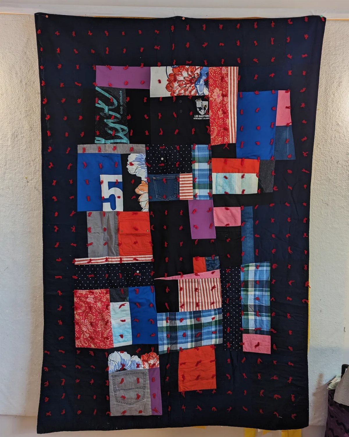 A dark navy patchwork quilt with colorful fabric squares hanging on a white wall.