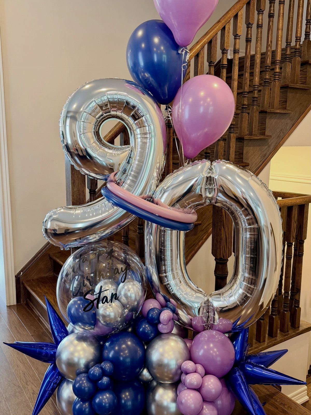 Silver number 90 balloons surrounded by blue, purple, and silver balloons near a wooden staircase.