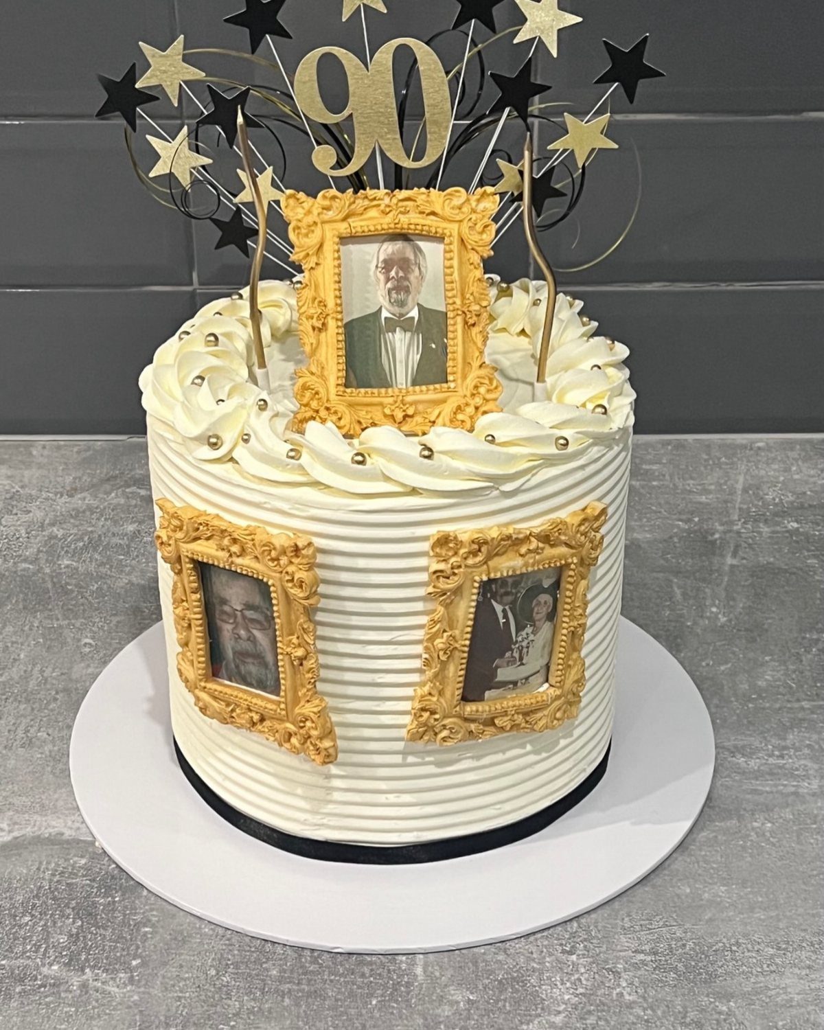 A white frosted birthday cake decorated with gold frames containing portraits and a 90 topper.