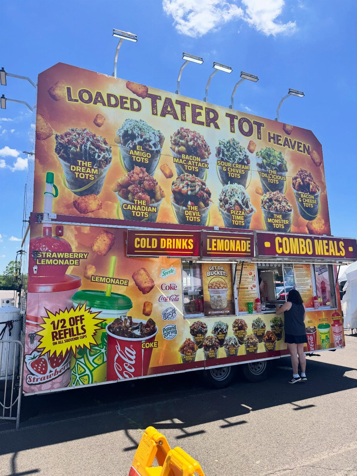 A colorful food truck advertising loaded tater tots and cold drinks under a blue sky.