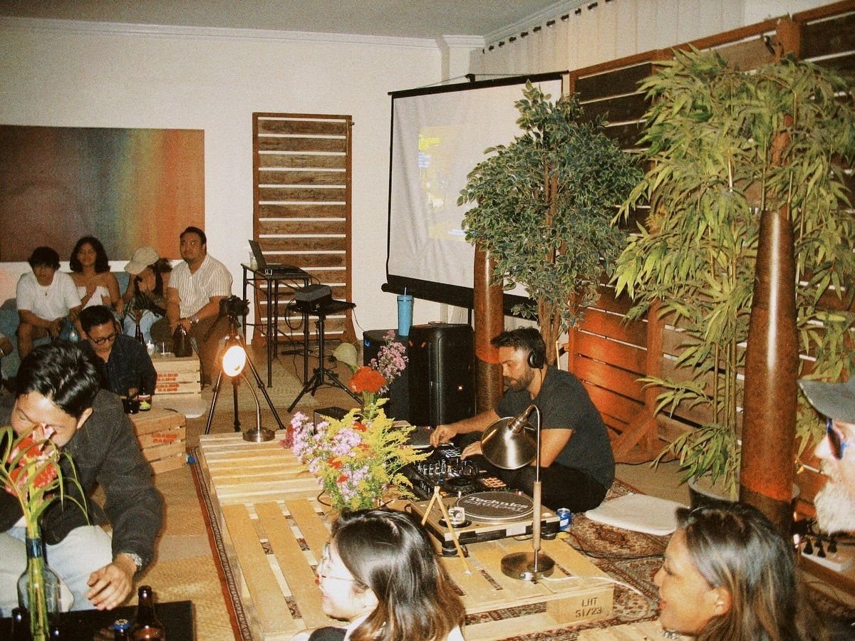 A DJ playing music on a turntable for a group of people sitting on floor platforms.