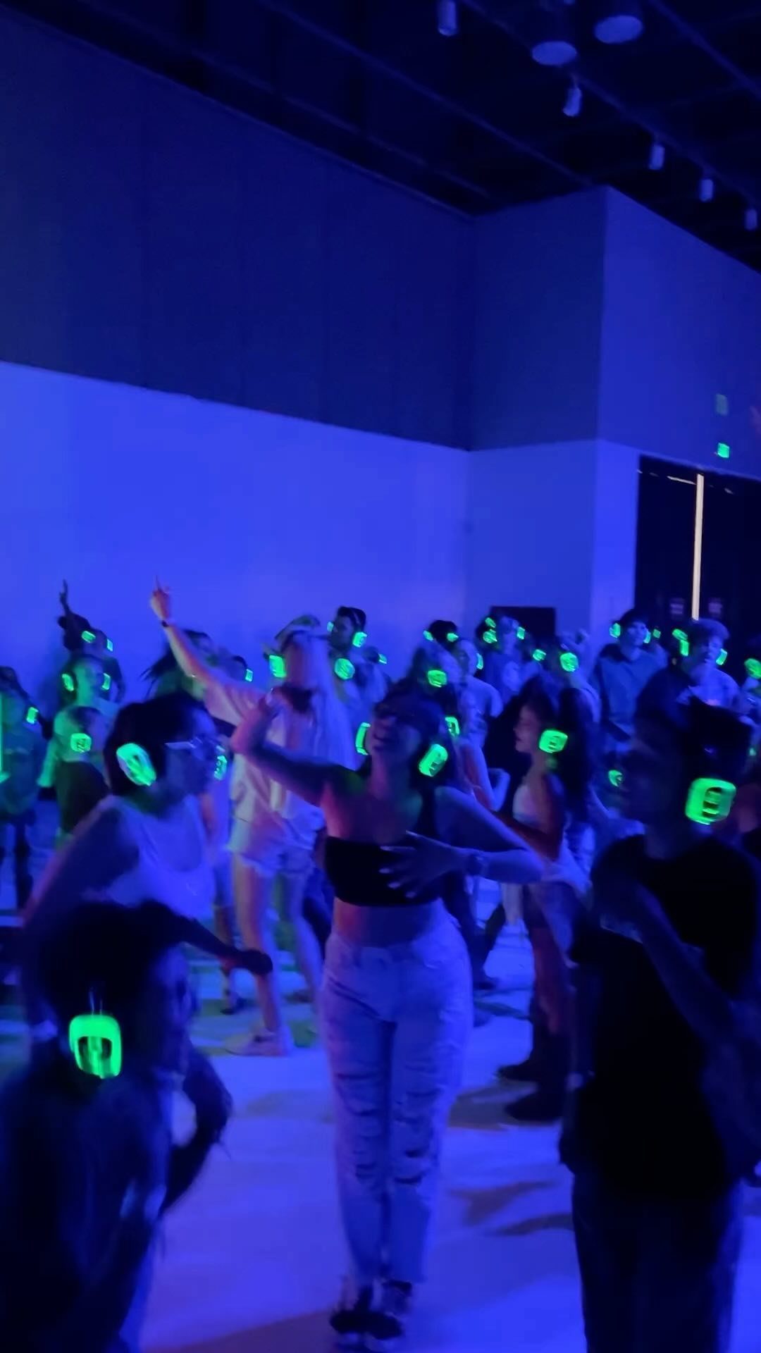 People dancing in a blue lit room wearing glowing green headphones during a silent disco.