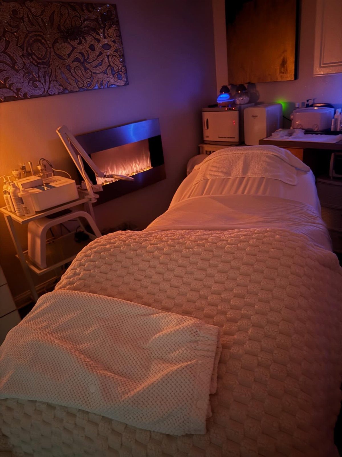 A massage table with pink textured blankets and white towels in a dimly lit room.