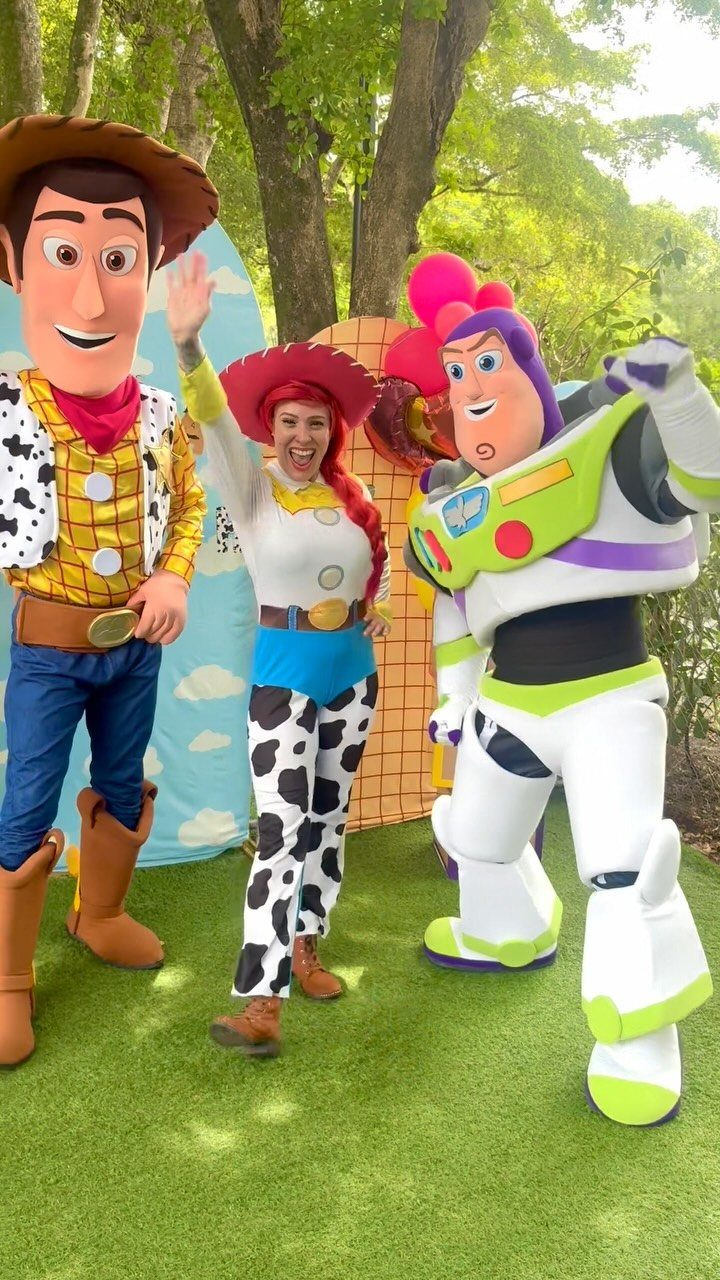 A woman in a Jessie costume posing between Woody and Buzz Lightyear mascots outdoors.