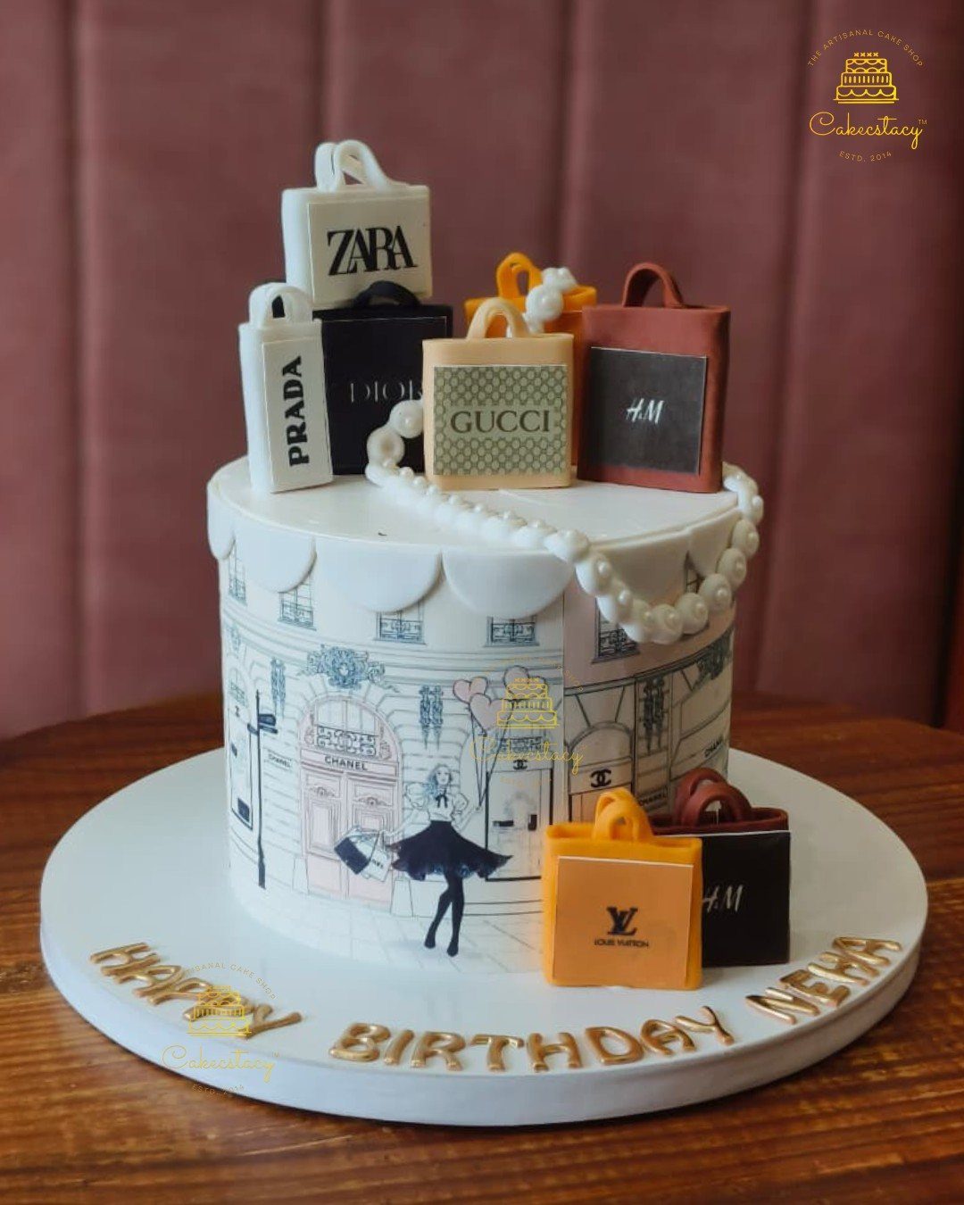A white designer themed cake topped with miniature luxury brand shopping bags and pearls.