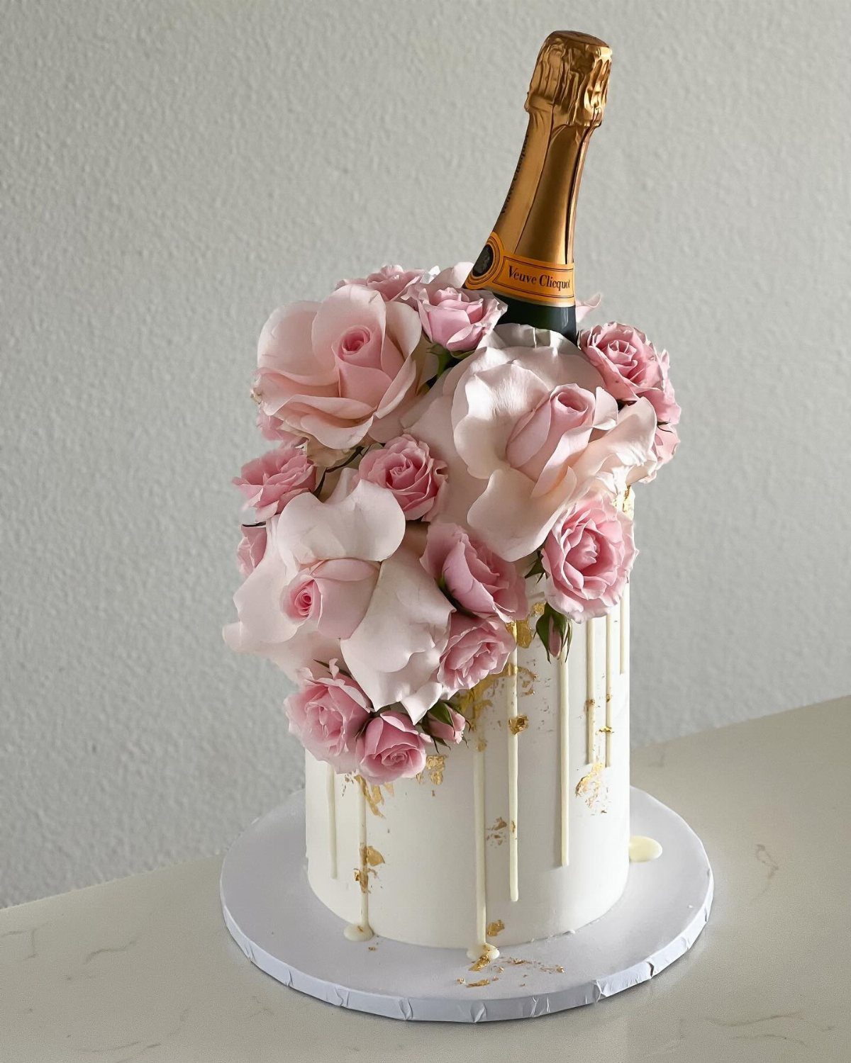 White cake decorated with pink roses and a champagne bottle with gold accents.