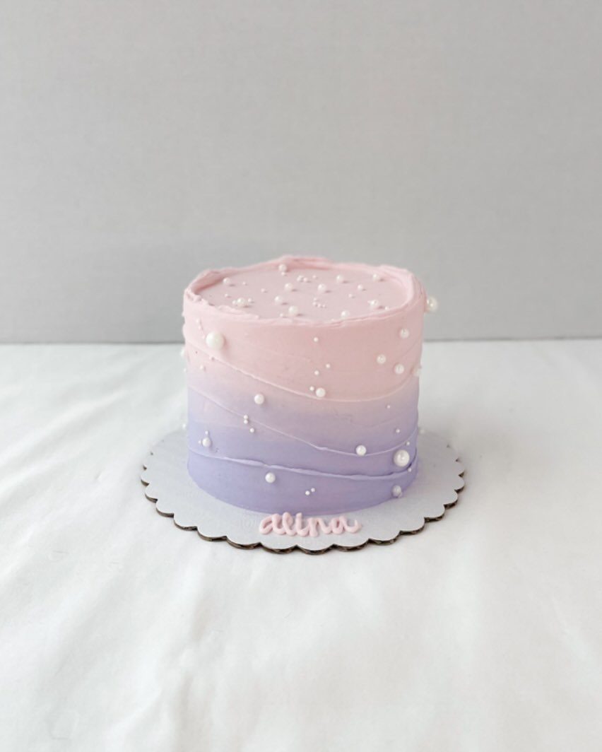 A single-tier ombre cake transitioning from light pink to lavender with white edible pearls.