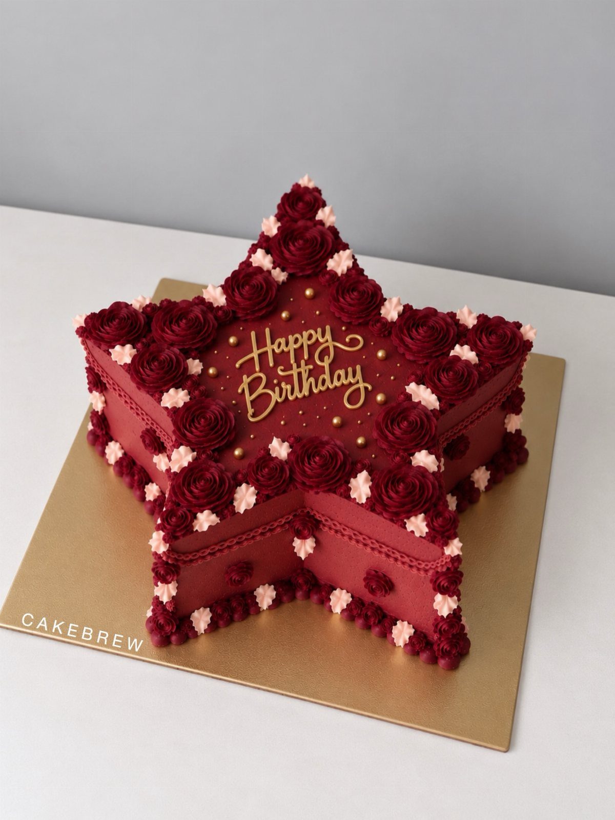 Star-shaped red cake decorated with burgundy buttercream roses and gold lettering on a gold base.
