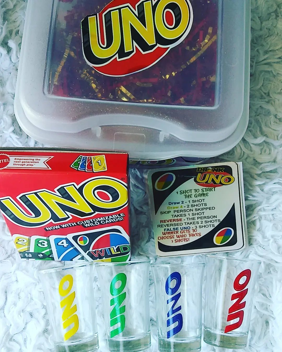 UNO card game, drinking game instructions, and four branded shot glasses on a white surface.