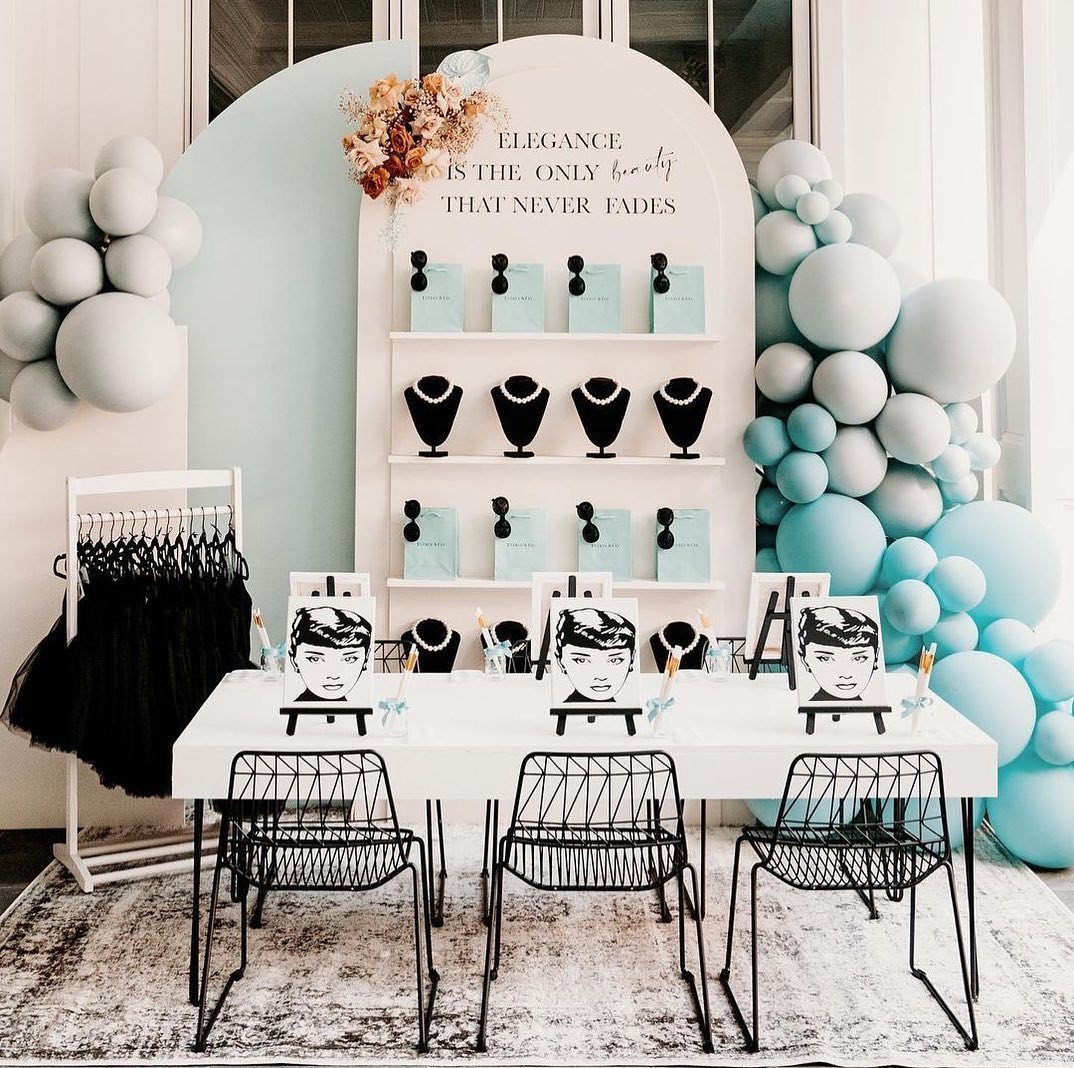 White display shelves with blue gift bags and necklaces set beside a decorated brunch table.