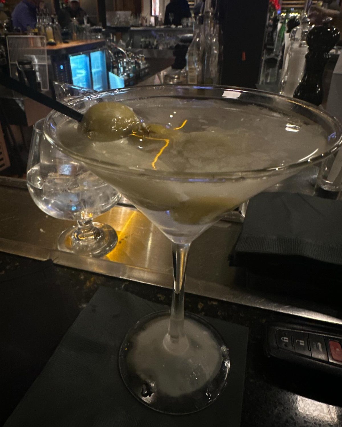 A dirty martini with green olives and ice served in a glass on a bar.