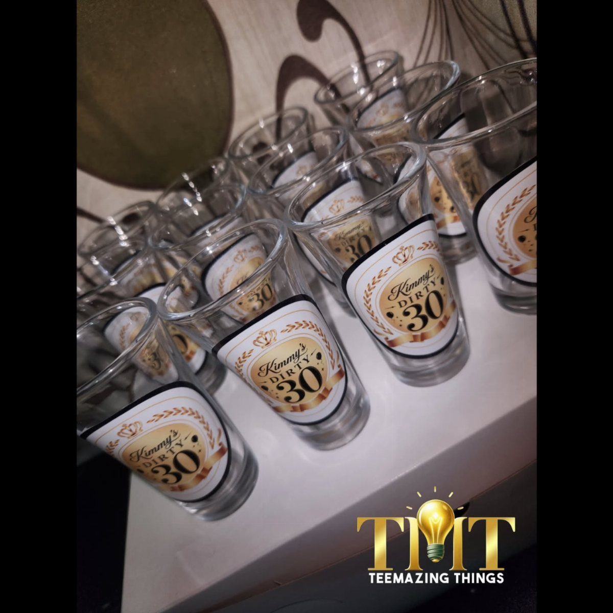 Clear plastic shot glasses with custom gold and white Dirty 30 labels arranged on a surface.