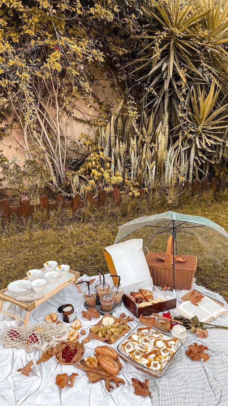 A picnic spread on a white blanket with pastries, bread, a wicker basket, and an umbrella.