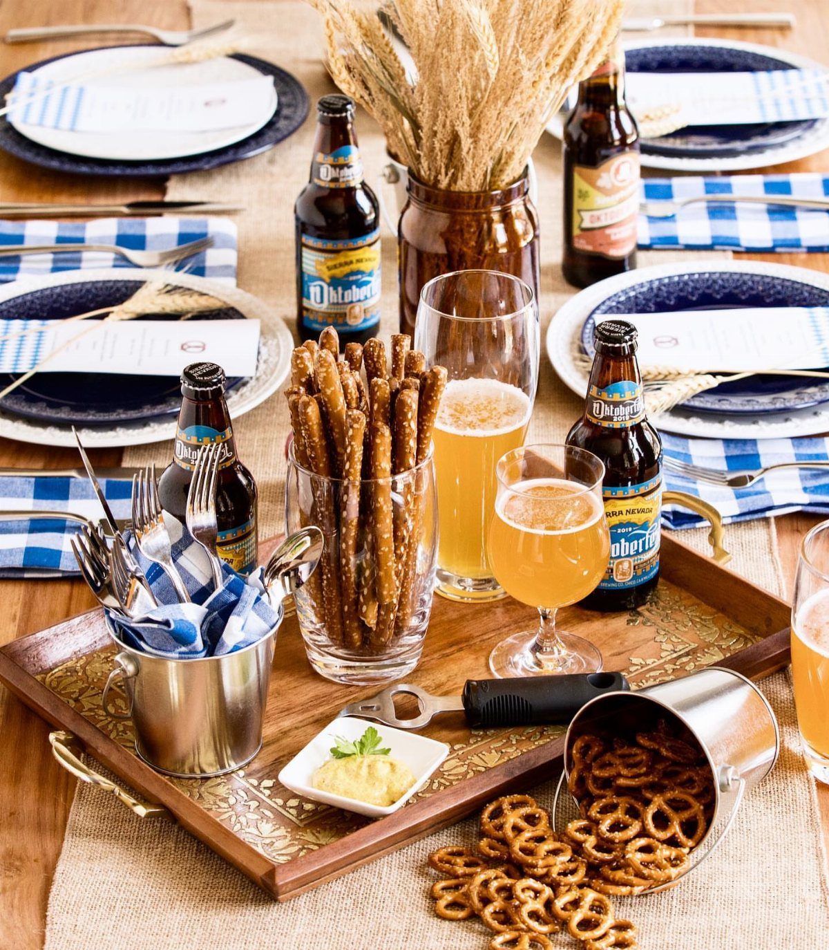 Beer bottles, glasses of beer, and pretzels arranged on a festive table with blue checkered napkins.