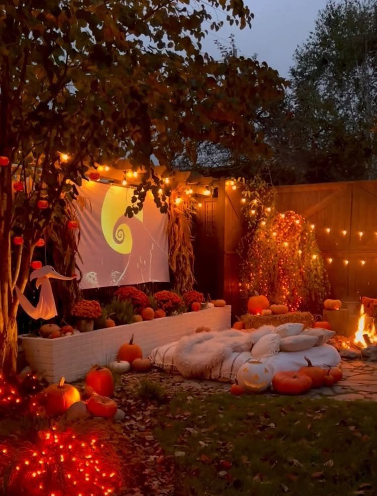 Outdoor movie setup with a projector screen, pumpkins, and cozy blankets in a backyard.