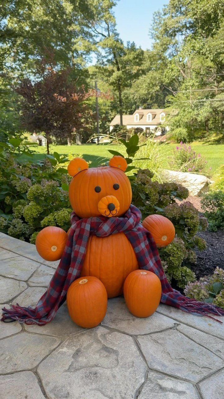 A large bear sculpture made from pumpkins wearing a plaid scarf on a stone patio.