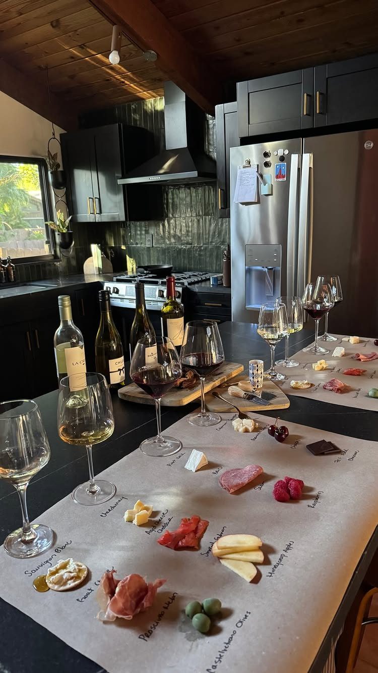Wine glasses and small appetizers like cheese and meat arranged on parchment paper on a kitchen counter.