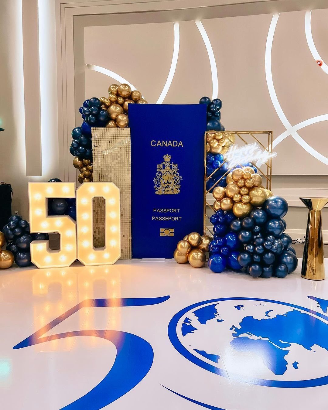 Large Canadian passport prop surrounded by gold and blue balloons and marquee number fifty.